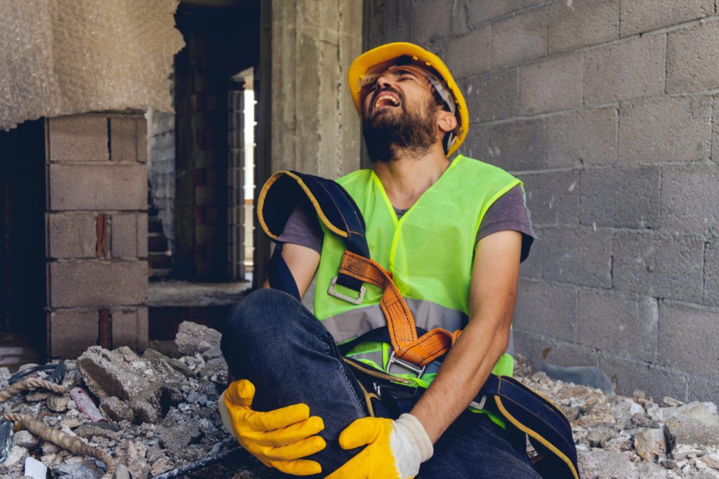 man with a yellow hard hat holding his leg in pain