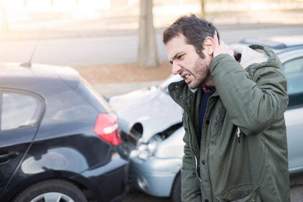 man in green jacket holding the back of his neck after a rear end car accident