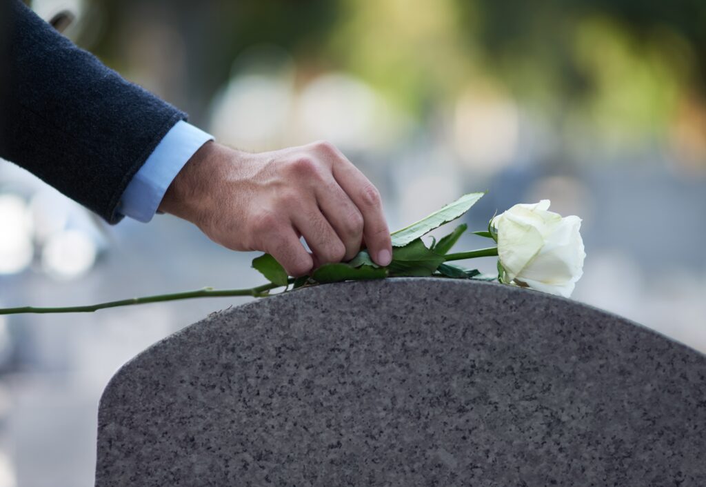 hand placing a white rose onto a gravestone