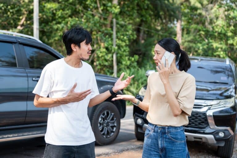 A man and a woman arguing after a car accident, with the woman contacting the other driver’s insurance company.