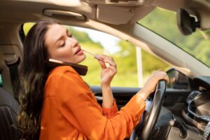 A woman dangerously distracted while driving, doing her makeup and talking on the phone.