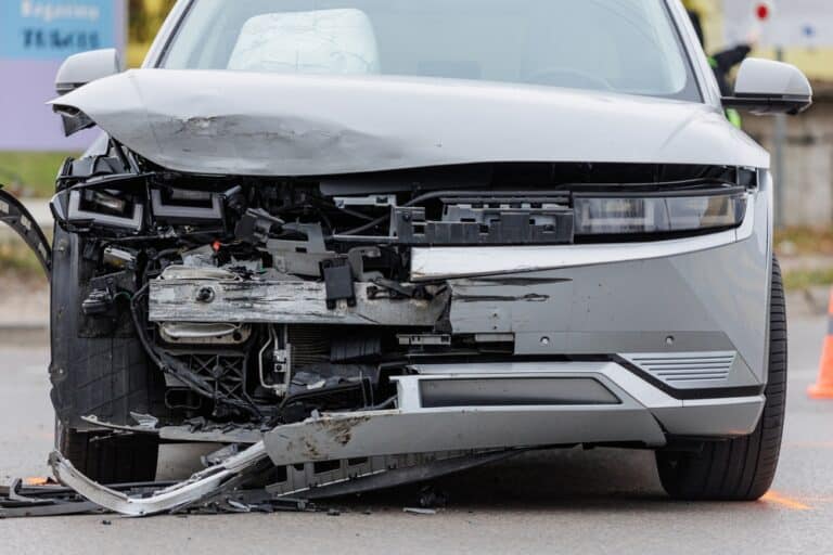 A smashed front end of a car after a car accident. Who can be sued?