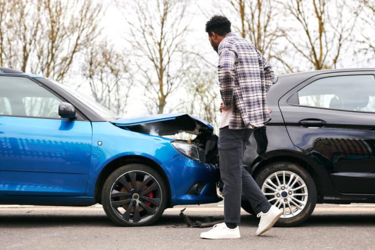 A man examining a rear-end collision that occurred during rush hour.