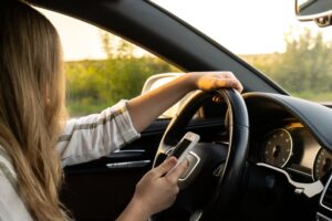 A woman using her smartphone while driving, researching the impact of smartphone use on overall crash rates.