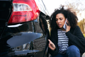 A woman looking at the damaged bumper of her car after a hit and run accident, wondering what to do.