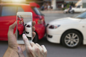 Someone using their phone to take a photo of their rear-end accident scene as they attempt to earn the average payout for a rear-end collision.