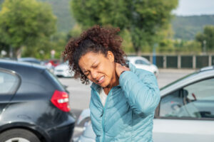 Woman holding her neck in pain while standing in front of two crashed cars while wondering, “When is a collision not your fault?”