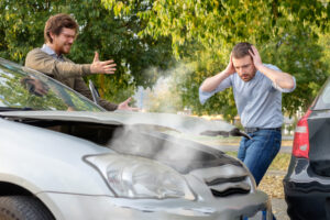 Two drivers stand next to their crashed cars and argue about who is at fault in a rear-end collision.