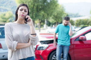 A woman on the phone with a man in the background after a parking lot accident, wondering what to do if there is no police report.