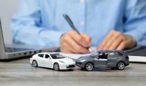 Model cars on a desk in front of a lawyer writing a client about whether it is too late to hire a car accident lawyer in Rhode Island.