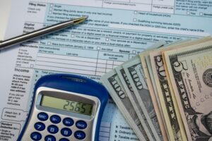 A stack of money next to a calculator on top of a tax return. Do you pay taxes on money from a lawsuit in Rhode Island?