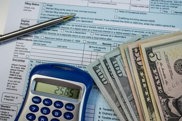A stack of money next to a calculator on top of a tax return. Do you pay taxes on money from a lawsuit in Rhode Island?