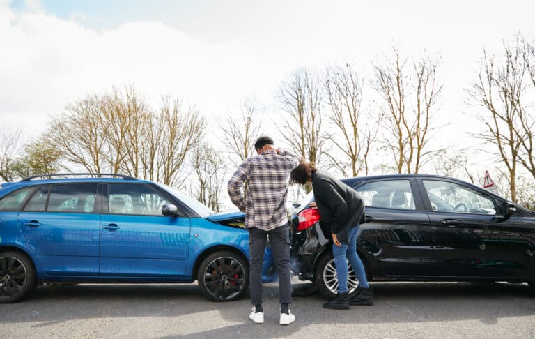A man and a woman looking at the damages in a rear-end car accident. What are the most common car accident injuries?